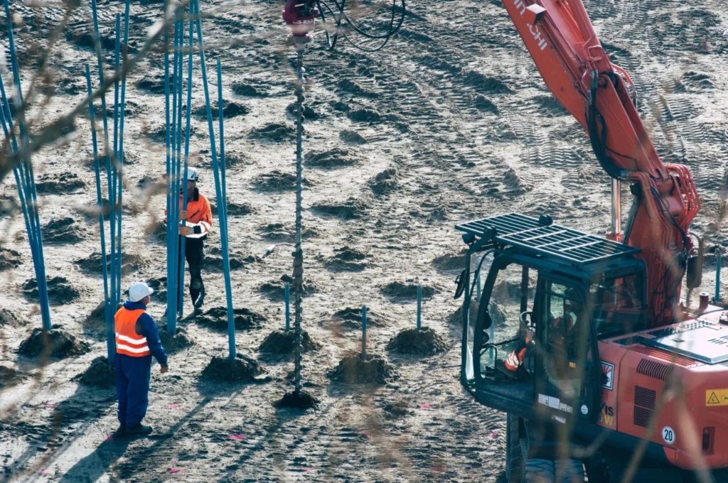 A construction site with workers and an excavator drilling holes in the ground.