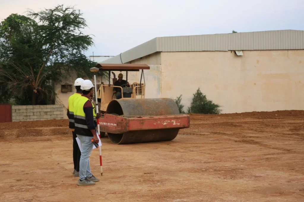Engineers in high-visibility vests supervise road construction with a roller.